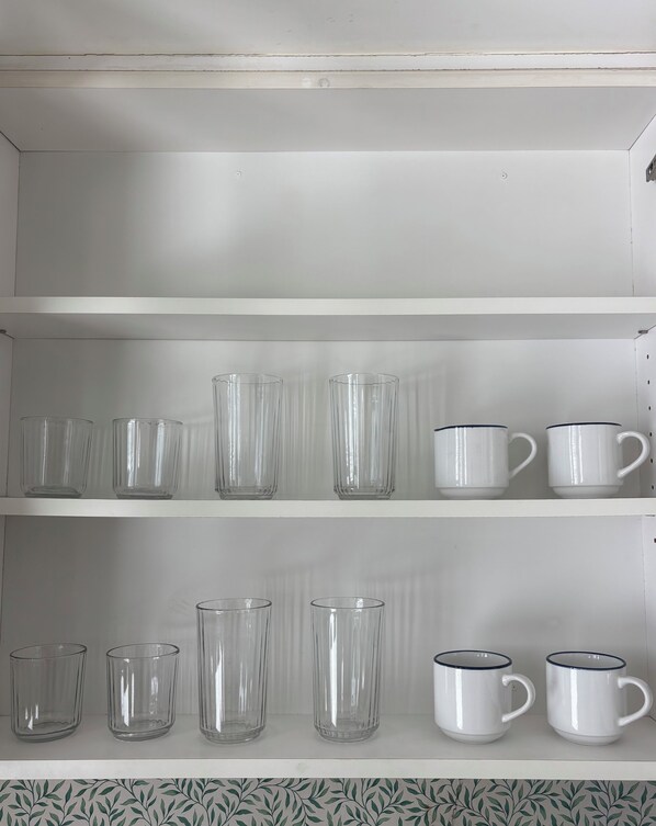 Un estante blanco con varias tazas de vidrio y cerámica.