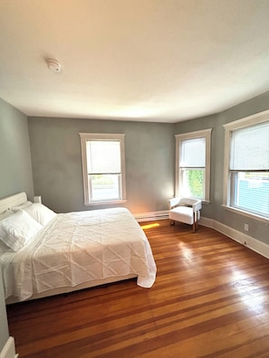 Un dormitorio con una cama, una silla y dos ventanas.