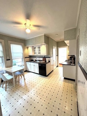 Una cocina con comedor, que presenta un piso de baldosas hexagonales, armarios blancos y un ventilador de techo.