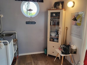 A compact kitchen with a sink, a cabinet with glass doors, a small table with a kettle, and a sign indicating a 500m distance to Plage. - New Listing (Dieppe)
