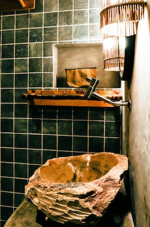 Une salle de bain avec un lavabo en pierre, une étagère avec une serviette et un luminaire suspendu.