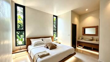 A modern bedroom with a large bed, a vanity with a mirror, and two windows with a view of greenery.
