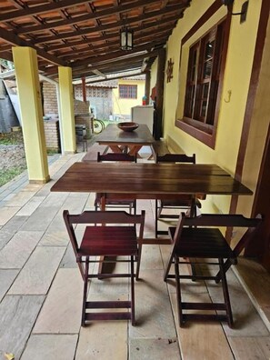 An outdoor patio with a wooden table and chairs, a yellow wall, and a brick floor. - Pousada Nevada Enseada (Ubatuba)