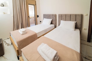 Una habitació d'hotel amb dos llits individuals, un sòl de fusta, una porta amb cortines i una taula petita amb una làmpada.