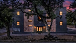 Een modern gebouw met een bakstenen gevel, huisnummer 214, met een centrale ingang met een deur en ramen, omgeven door bomen.