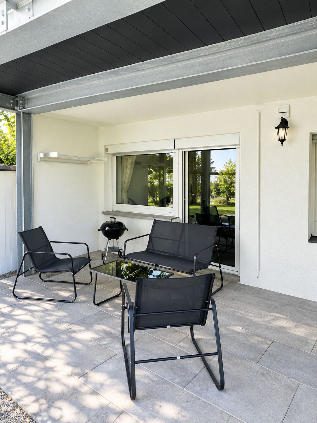 Un patio exterior con una mesa de vidrio, dos sillas negras y una parrilla.