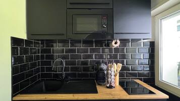 A modern kitchen with black cabinets, a black tiled backsplash, a wooden countertop, and a window with a view.