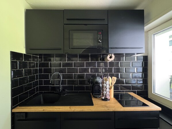 A modern kitchen with black cabinets, a black tiled backsplash, a wooden countertop, and a window with a view.