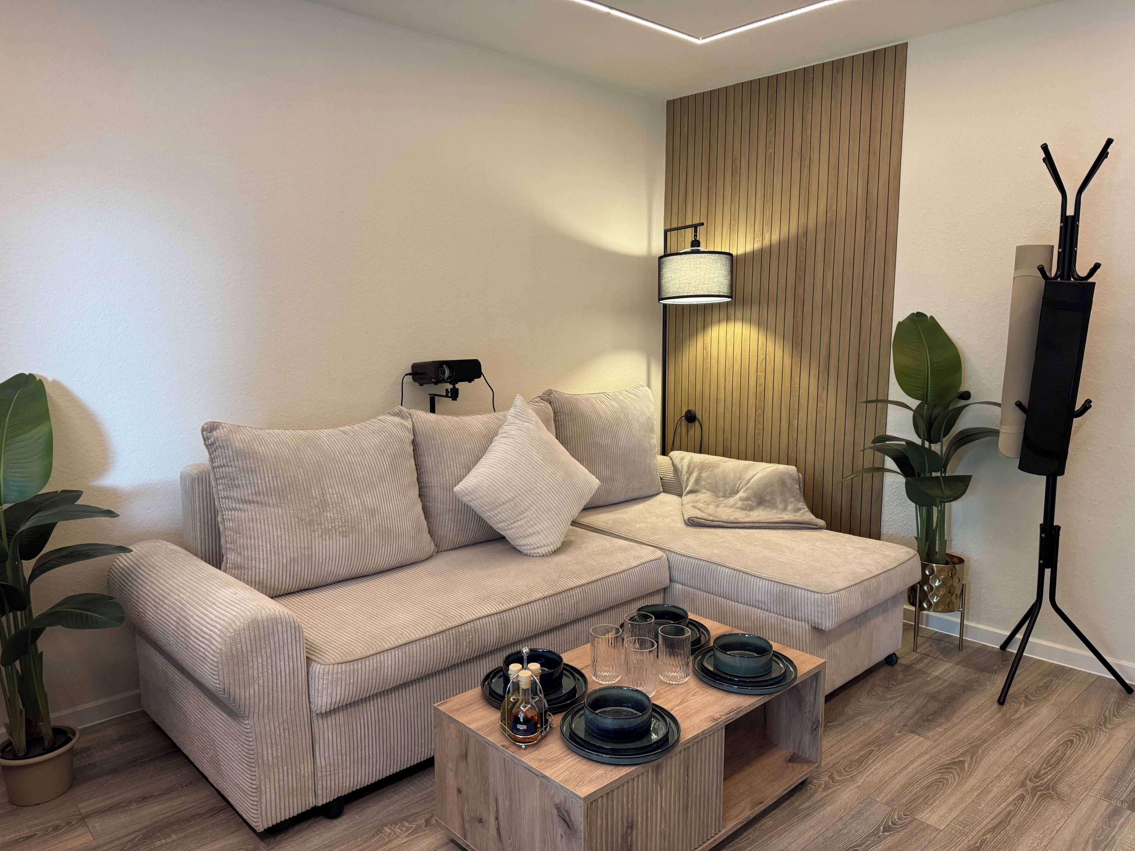 A modern living room with a sectional sofa, a wooden accent wall, a standing lamp, and a coffee table with decorative items.