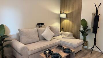 A modern living room with a sectional sofa, a wooden accent wall, a standing lamp, and a coffee table with decorative items.