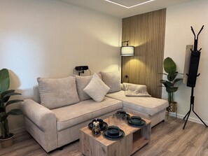 A modern living room with a sectional sofa, a wooden accent wall, a standing lamp, and a coffee table with decorative items.