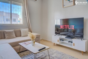 A modern living room with a large flat-screen TV displaying the Netflix logo, a beige sofa, a white coffee table with a magazine, and a decorative vase. - Marvelous 2-bedroom apartment in Agadir perfect for your getaway (agadir)