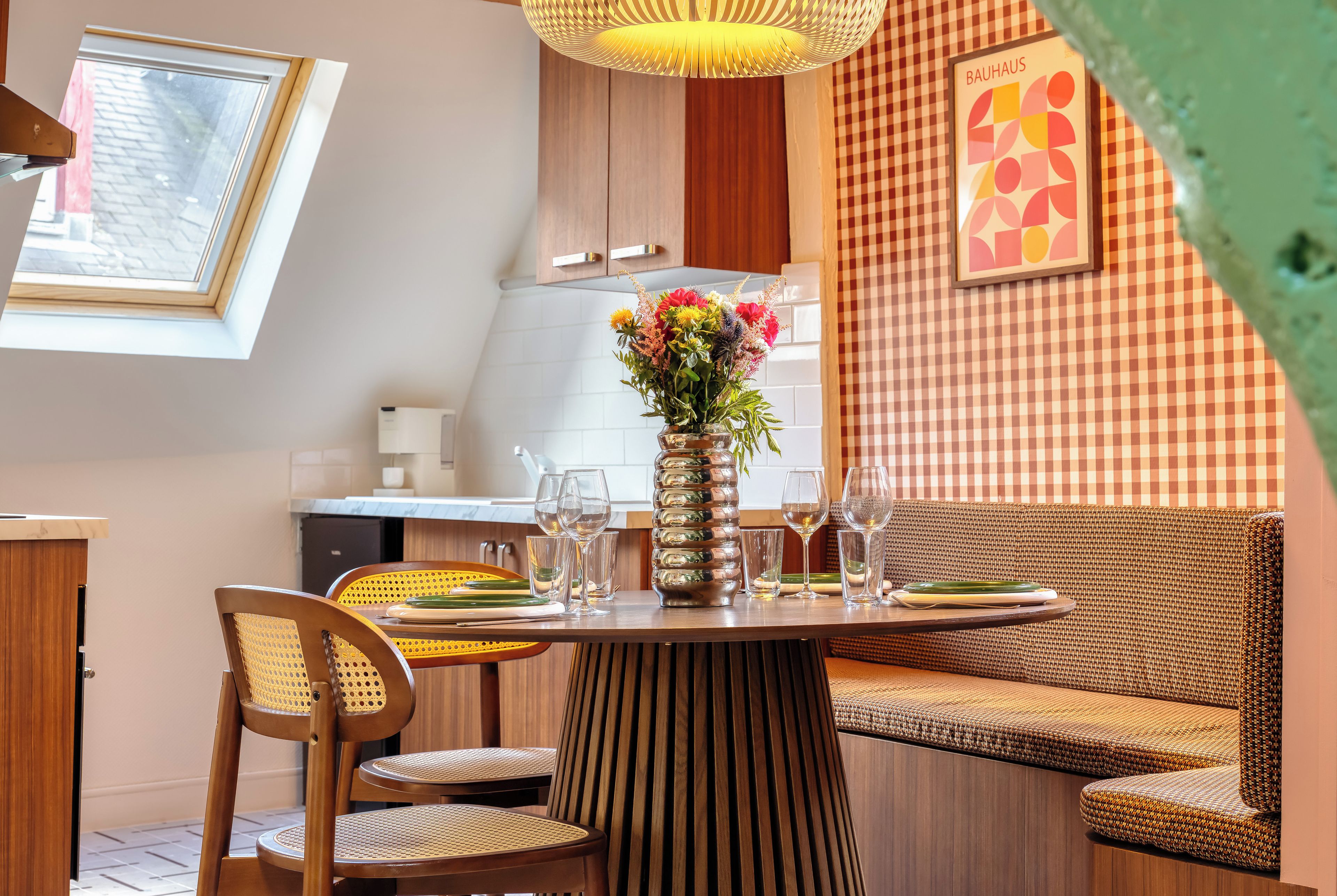 A dining area with a round table, chairs, a vase with flowers, and a checkered wall.
