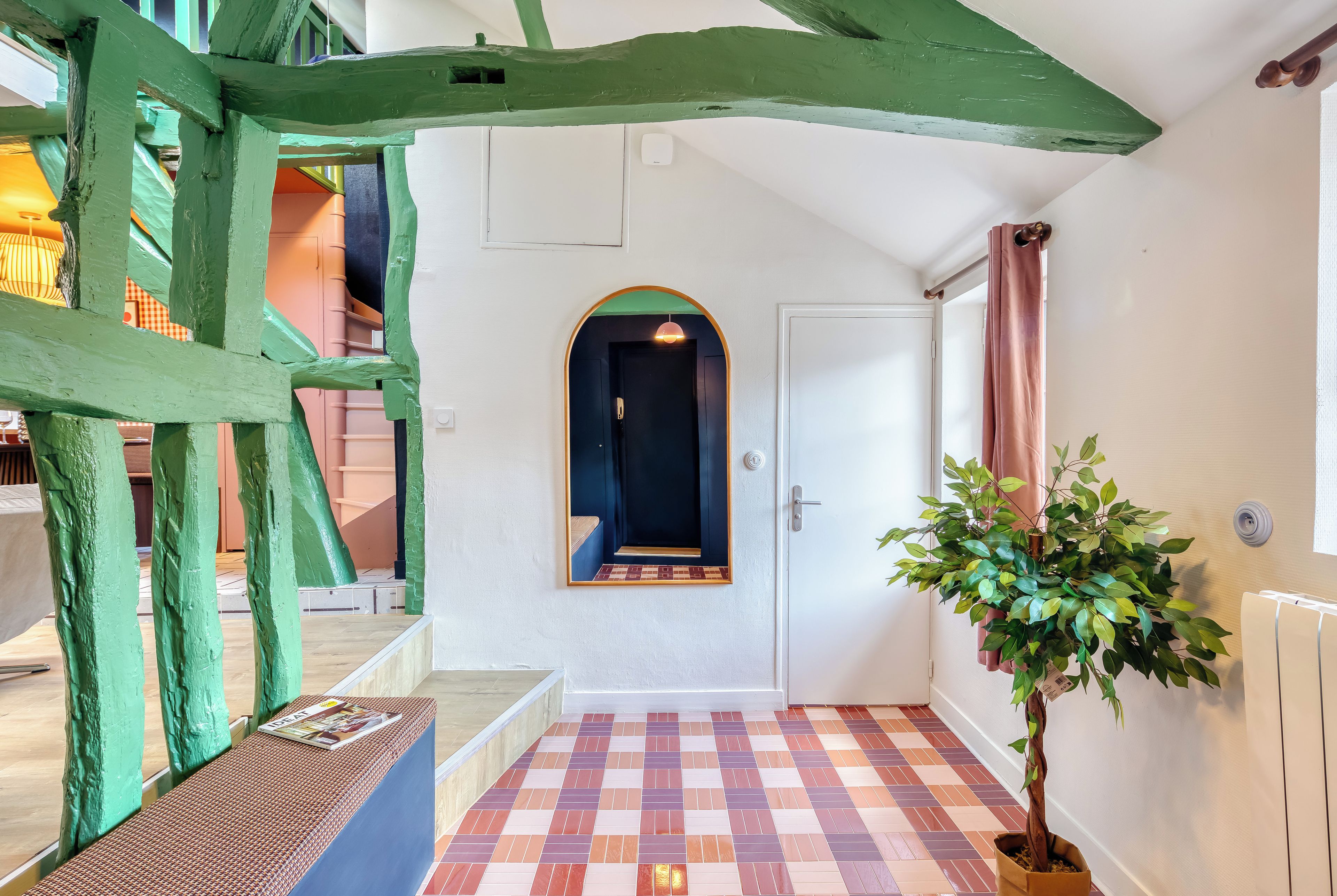 A hallway with a checkered floor, a door with a mirror, and a potted plant.