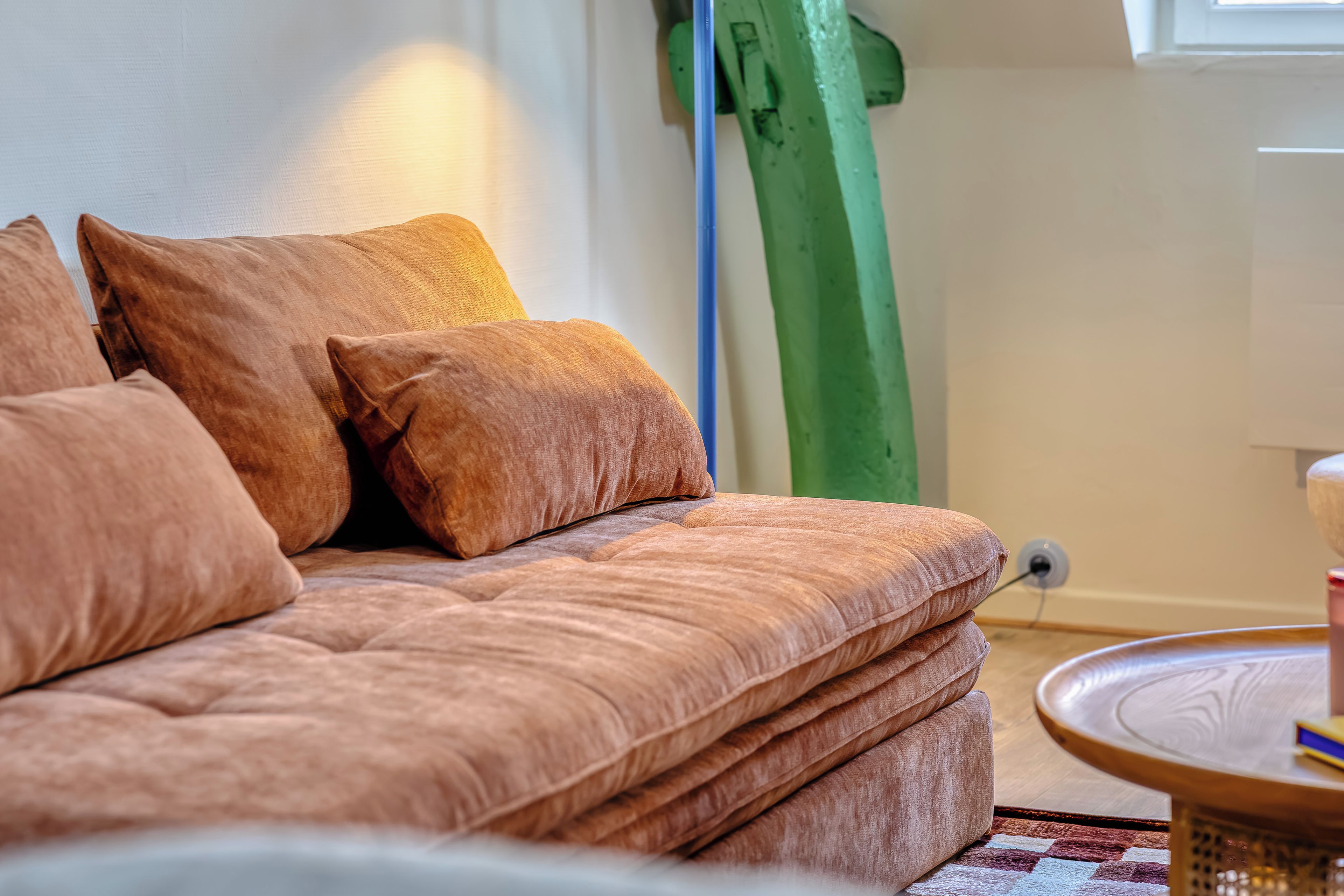 A sofa with multiple cushions, a round side table, and a green vertical object in the background.