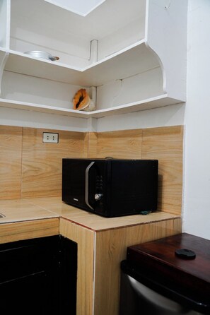 Een compacte keuken met een magnetron op een houten aanrecht, een klein spoelbakje en een kast erboven.