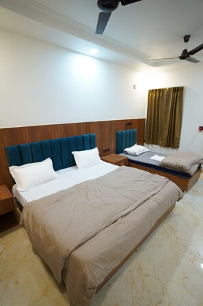 A hotel room with a large bed, a wooden headboard, a bedside table, a nightstand, and a ceiling fan. - AMANTA VEDA powered by Conara Connect (Varindavan)