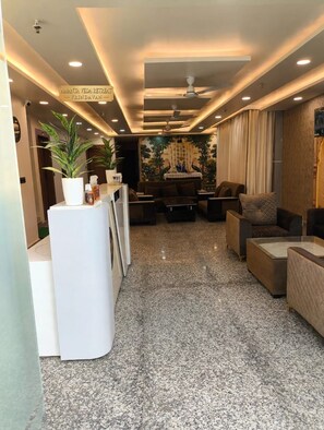 Um saguão de hotel com balcão de recepção, área de estar e uma parede decorativa.