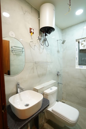 A bathroom with a white sink, toilet, and shower. There is a mirror above the sink and a towel rack. - AMANTA VEDA powered by Conara Connect (Varindavan)
