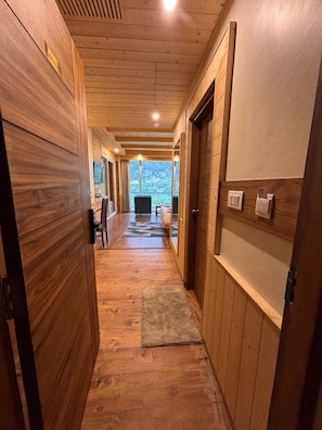 A wooden hallway leading to a room with a bed and a view of the outdoors. - The Ravasa (Manali)
