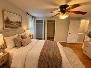 Un dormitorio con cama, mesitas de noche, ventilador de techo y un cuadro en la pared.