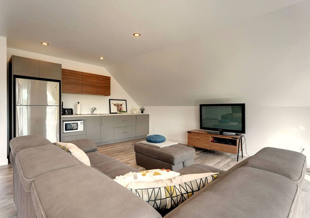 A modern living room with a sofa set, a television, and a kitchen area with cabinets and a microwave.