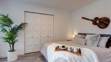 A bedroom with a bed, a guitar wall art, a plant, and a door.