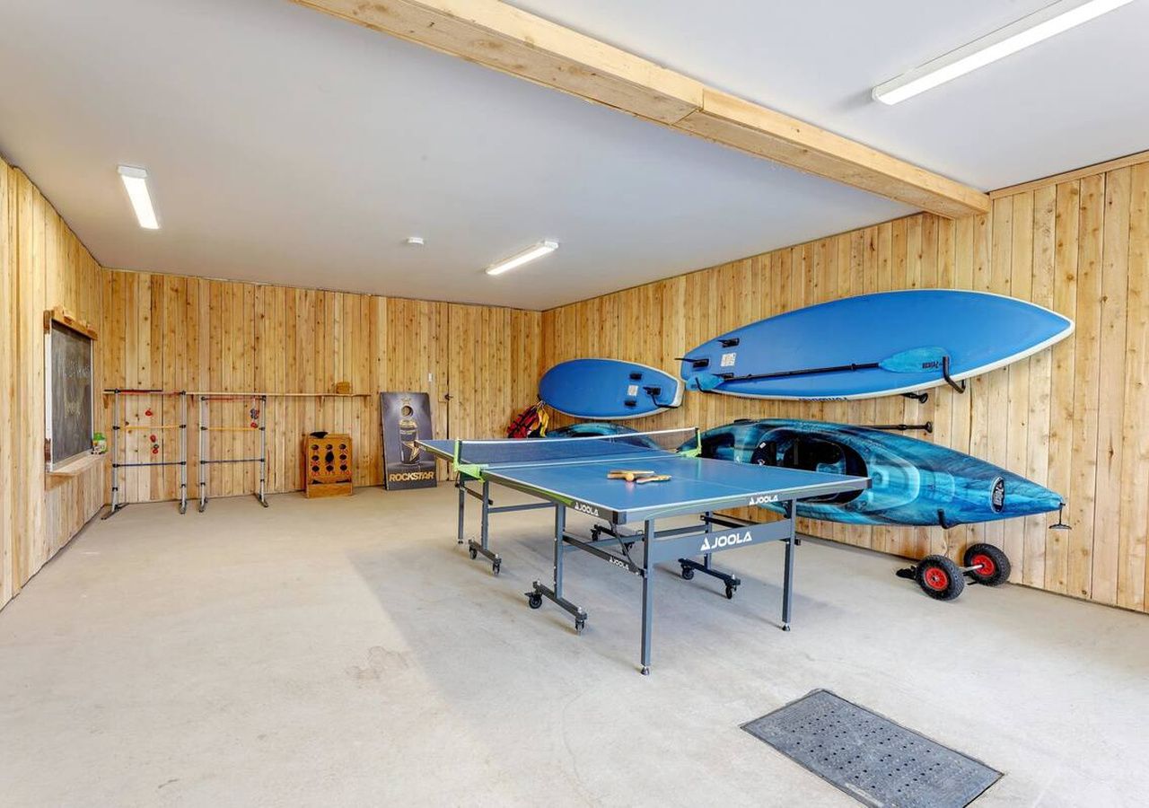 A ping pong table in a room with wooden walls, a blue paddle, and a blue paddleboard.