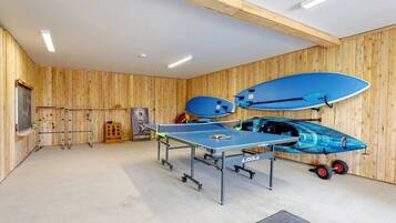 A ping pong table in a room with wooden walls, a blue paddle, and a blue paddleboard.