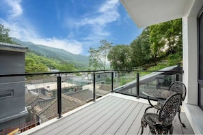 A balcony with a view of a mountainous landscape, a table with chairs, and a glass railing. - xiang zi zai homestay (Huairou)