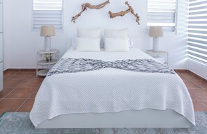 Una cama con colcha blanca acolchada, dos mesitas de noche con lámparas, y un adorno decorativo sobre la cama.