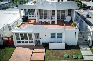 Una casa moderna de dos pisos con un patio, una zona de estar techada al aire libre y una entrada con portón.