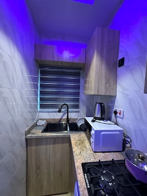 Cocina compacta con estufa a gas, pileta, horno integrado y ventana con persianas.