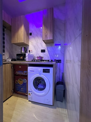 A compact kitchen with a washing machine, a microwave, and a coffee maker. - Elara Unit—Secure, Stylish 1-bed in Lagos — 24/7 power AC, Wi-Fi & full kitchen (Lagos)