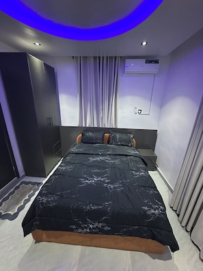 Un dormitorio moderno con cama, armario, mesita de noche y aire acondicionado de pared.