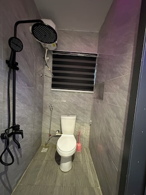 Un baño con inodoro, cabezal de ducha y ventana.