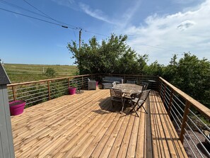 Une terrasse en bois, dotée de mobilier d’extérieur, d’une rambarde et offrant une vue sur la campagne.