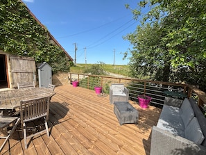 Une terrasse en bois avec des meubles d’extérieur, un petit abri de jardin et un espace clos agrémenté de verdure.
