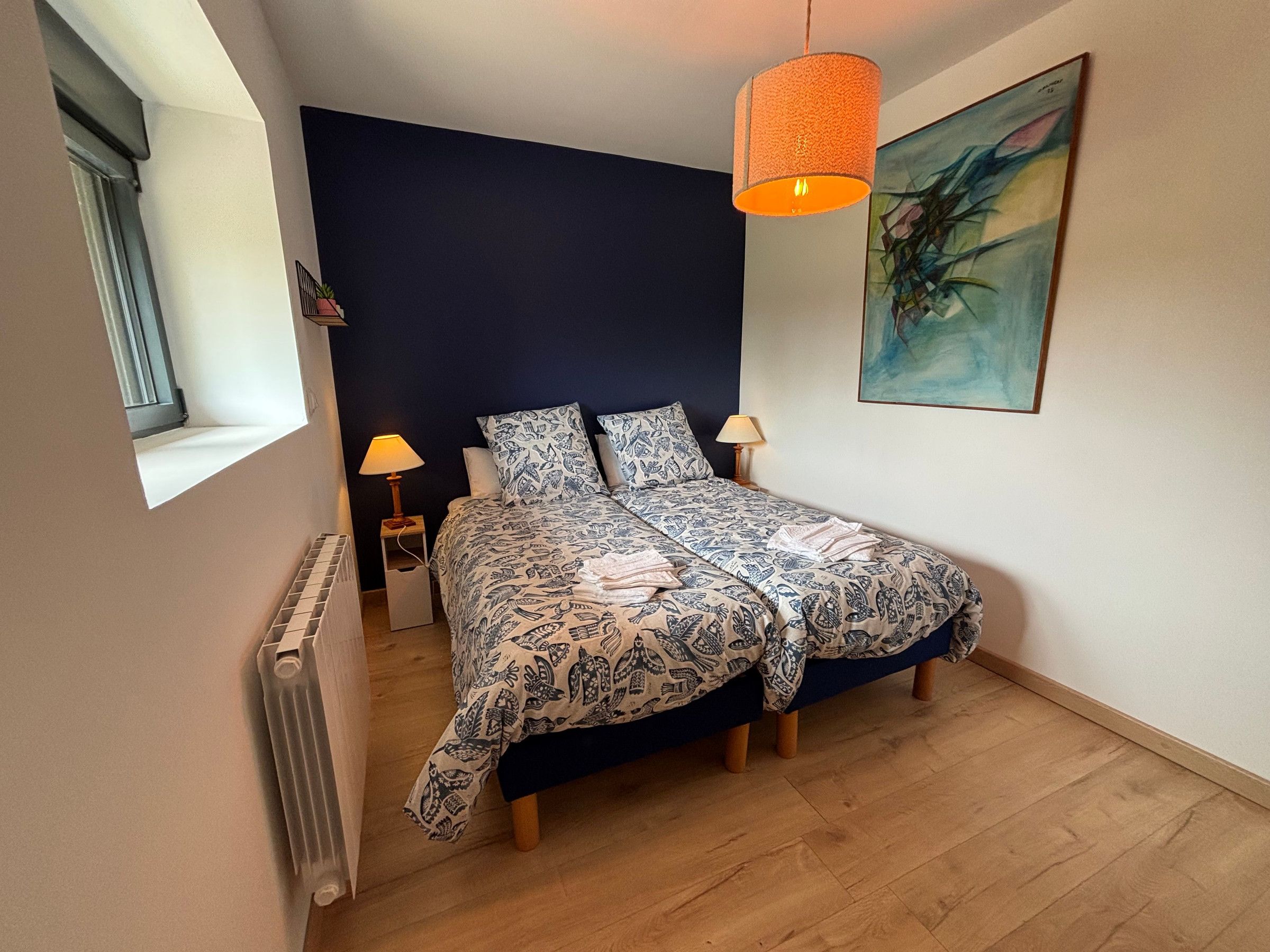 Een slaapkamer met een bed, twee bedlampen, een radiator en een schilderij aan de muur.