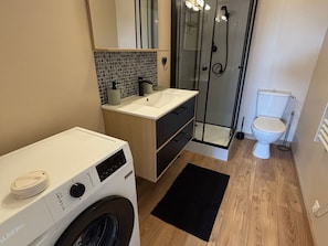 Une salle de bain moderne équipée d’un lave-linge, d’une douche à parois de verre et de toilettes.