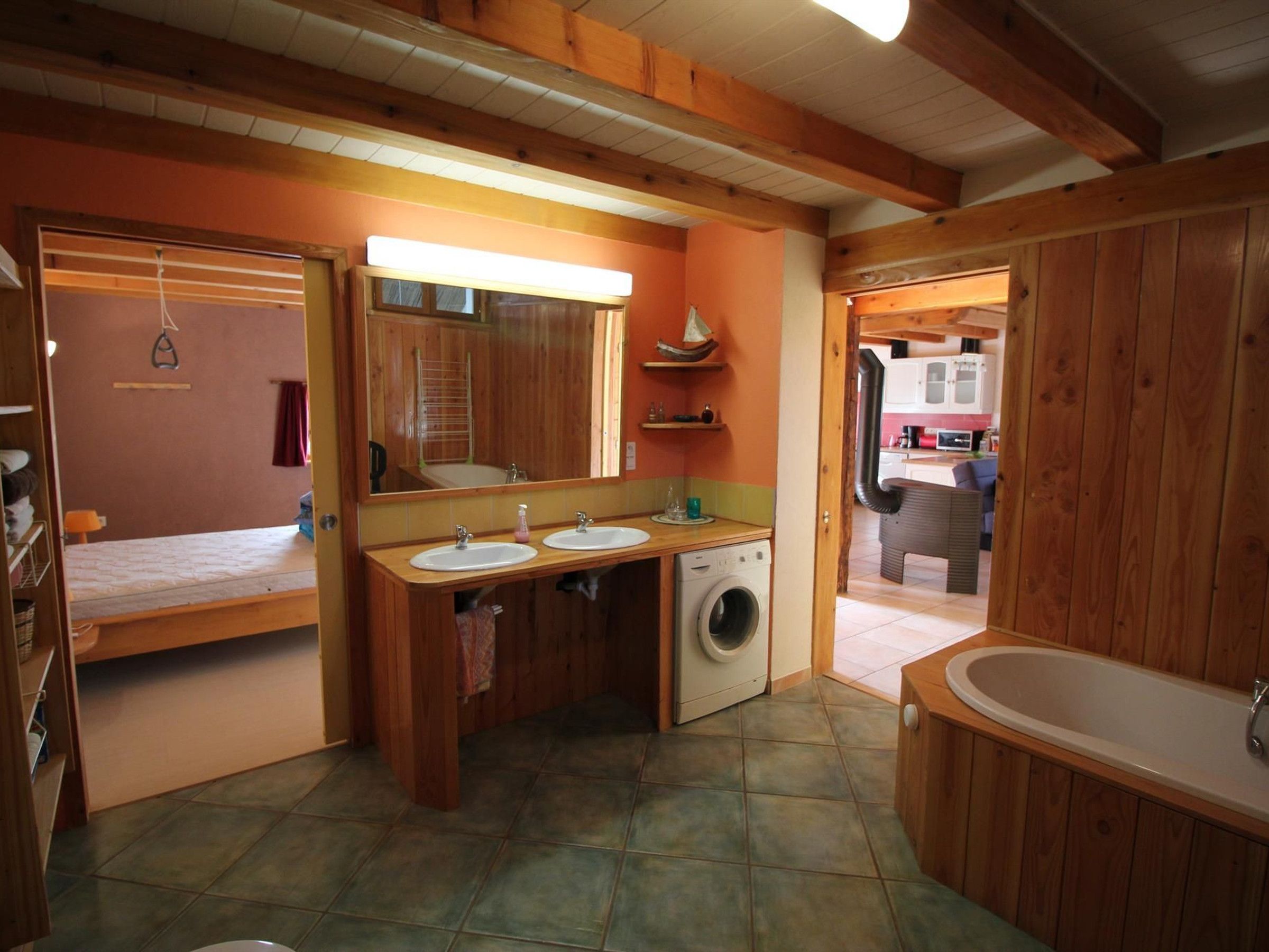 Un baño con paredes de madera, un espejo grande, dos lavamanos, una lavadora y una bañera.