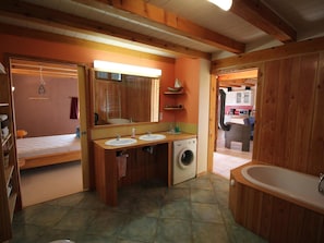 A bathroom with wooden walls, a large mirror, two sinks, a washing machine, and a bathtub.