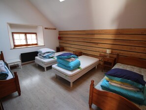 A dormitory room with two single beds, a small table, a radiator, and a window with blinds.