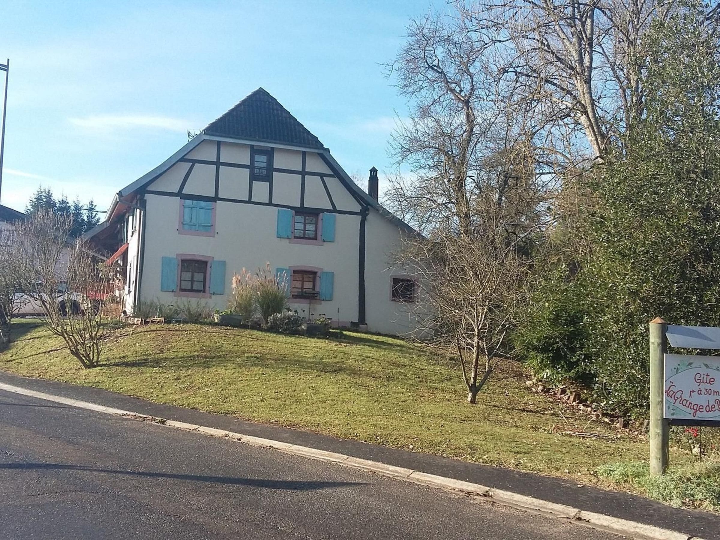 Et traditionelt bindingsværkshus med skråt tag, en lille have og et skilt foran.