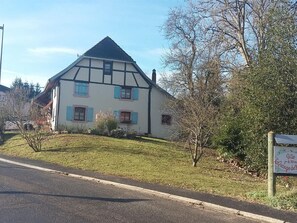 A traditional half-timbered house with a sloped roof, a small garden, and a signboard in front.