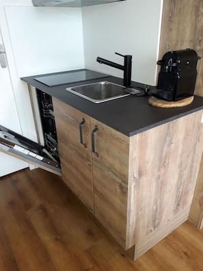 Een kleine keuken met een ingebouwde vaatwasser, een spoelbak en een koffiezetapparaat op het aanrecht.