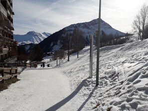 Een besneeuwde piste met een berg op de achtergrond, een houten hek en een gebouw aan de linkerkant.