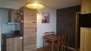 Een kleine keuken met een inbouwfornuis, houten kastjes en een eethoek met een tafel en stoelen.