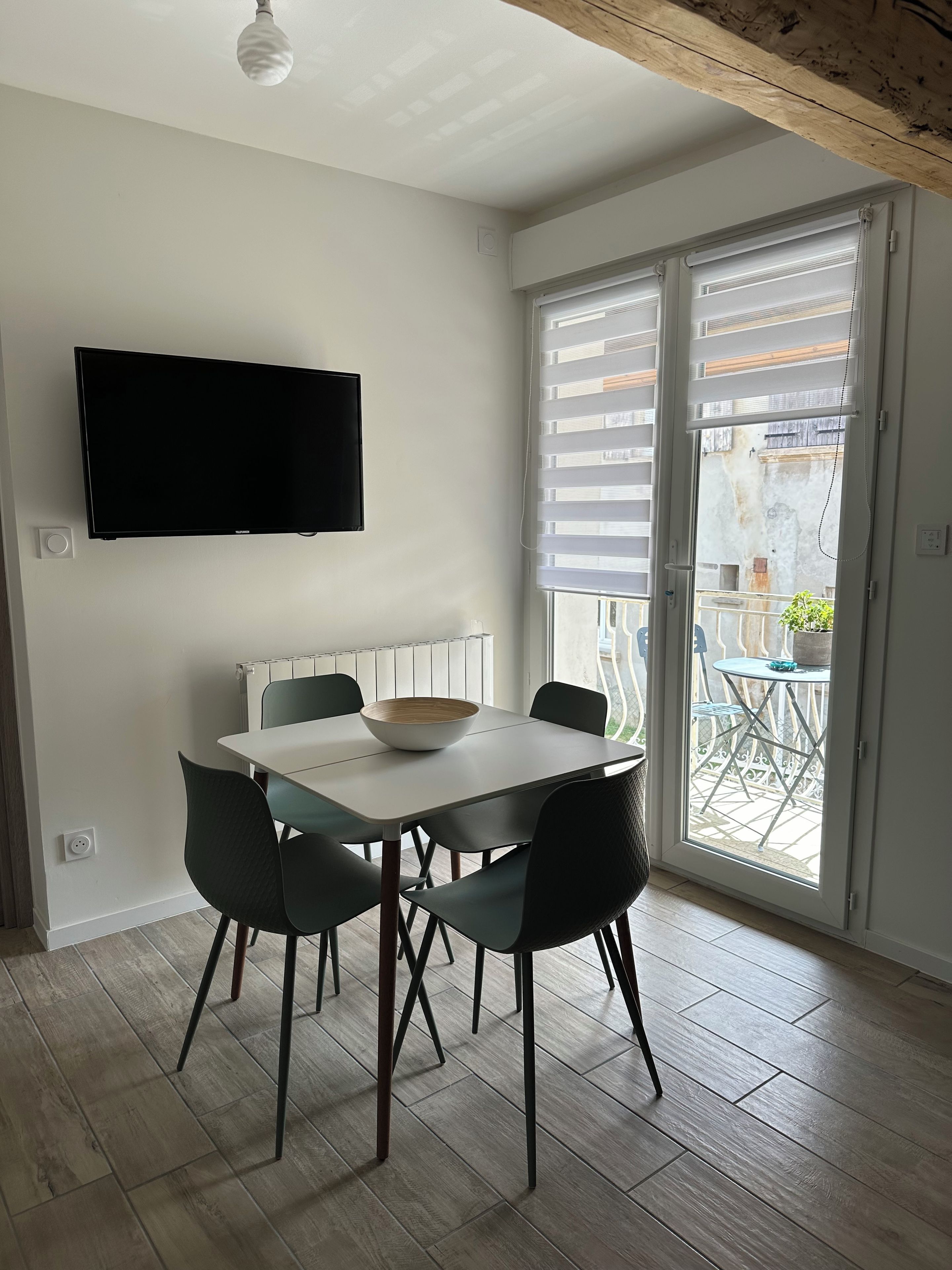 A dining area with a table, chairs, a bowl, a flat-screen TV mounted on the wall, and a sliding glass door leading to an outdoor balcony.