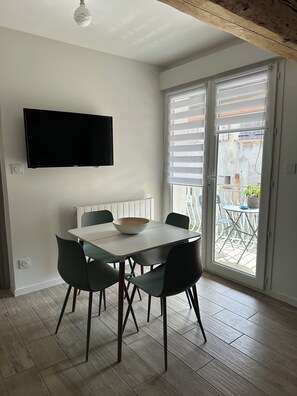 Un coin repas comprenant une table, des chaises, un saladier, un téléviseur à écran plat fixé au mur et une porte-fenêtre coulissante donnant sur un balcon extérieur.